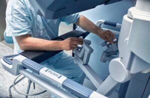 Healthcare professional in scrubs seated at a large medical device, adjusting control levers and handles.