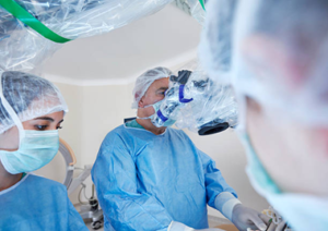 Surgical team in blue gowns, masks, and caps performing an operation in an operating room.